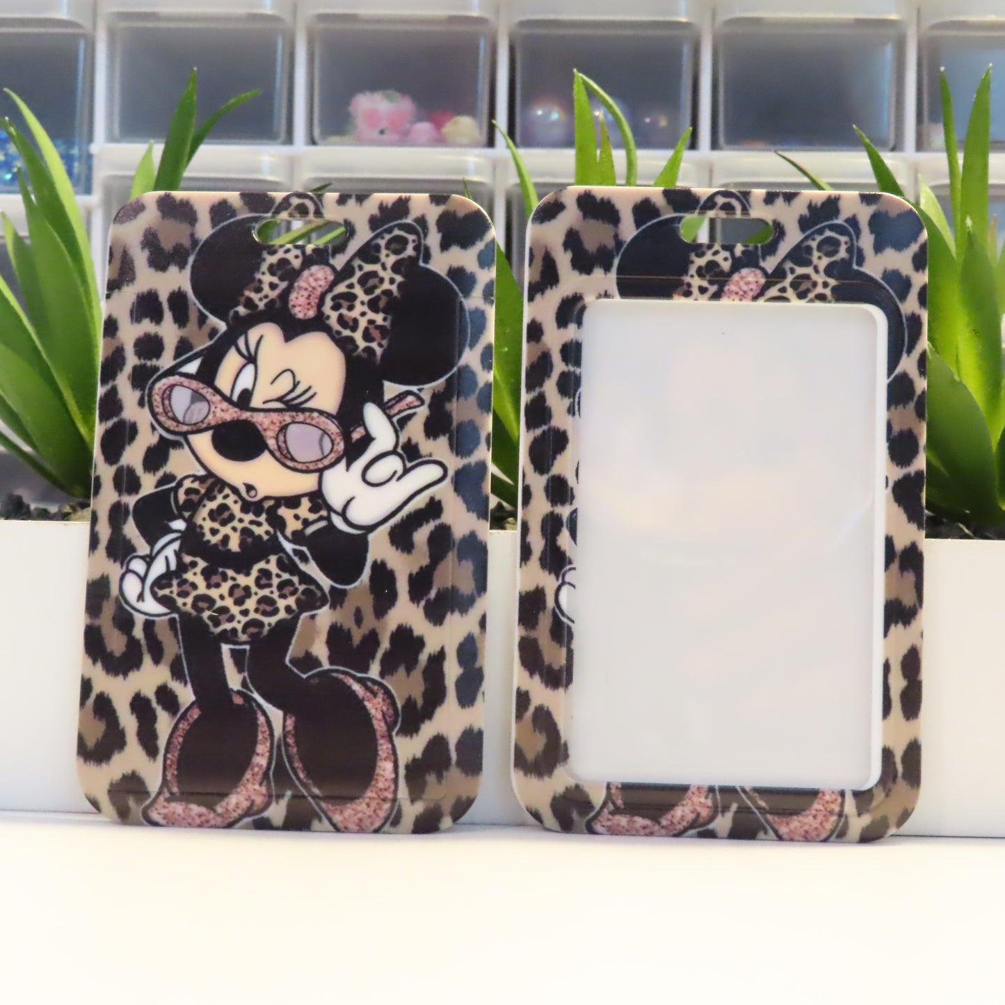 Phone case with leopard print design featuring a character, placed on a white surface with green plants in the background.