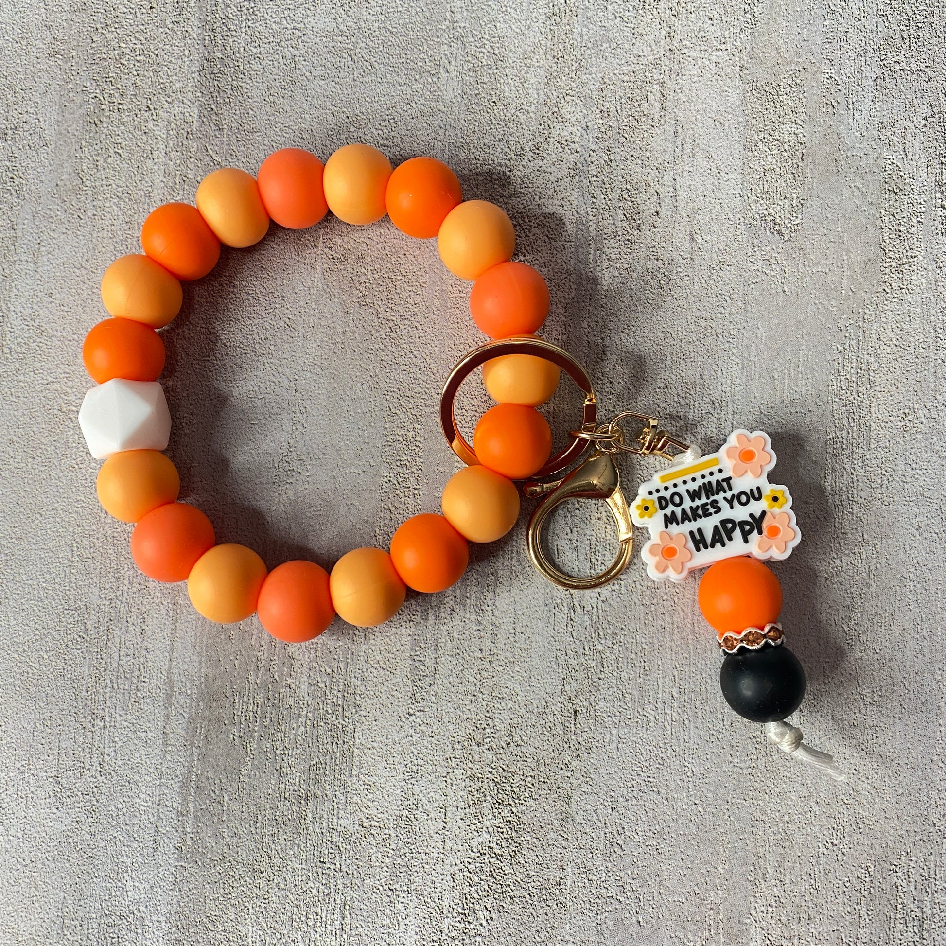 Beaded keychain with orange, yellow, and white beads on a textured gray surface.