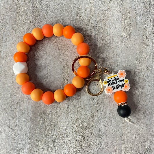 Beaded keychain with orange, yellow, and white beads on a textured gray surface.