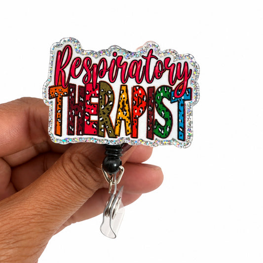 A hand holding a die-cut sticker that reads 'Respiratory Therapist' in colorful glittery letters with a holographic silver border, attached to a black retractable clip.