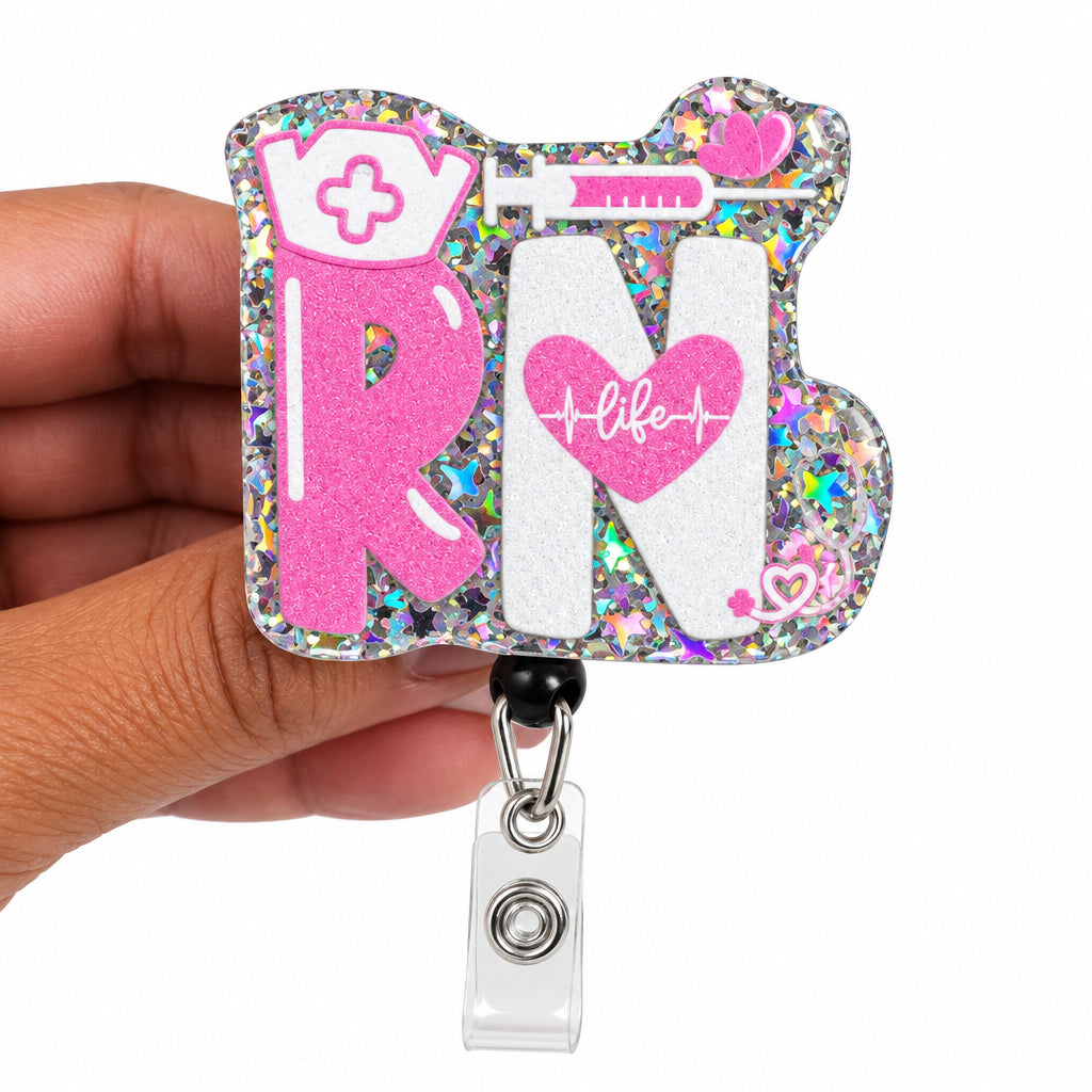 A hand holding a custom holographic acrylic badge reel featuring the letters 'RN' in pink and white with a heart and syringe design, complete with a clear plastic clip.