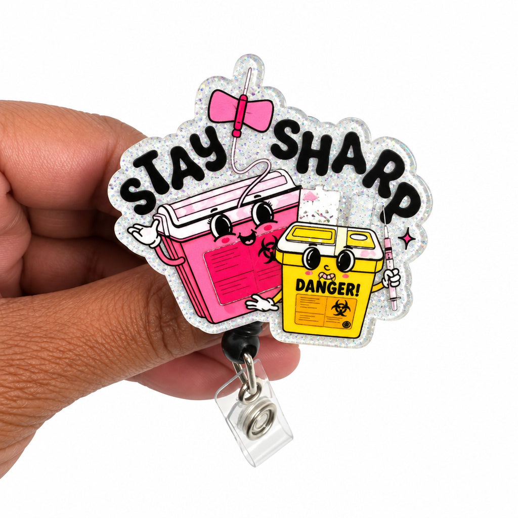 A hand holding a die-cut acrylic badge reel featuring the phrase 'STAY SHARP' in black letters above two cartoon books, one pink and one yellow with a 'DANGER!' label, on a plain white background.