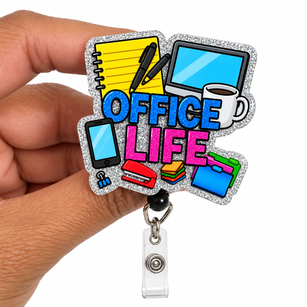 A hand holding a glittery 'Office Life' badge reel. The badge features colorful icons of office items (laptop, mug, phone, notebook) and the words 'OFFICE LIFE' in blue and pink glitter lettering, with a silver metal clip attached at the bottom.