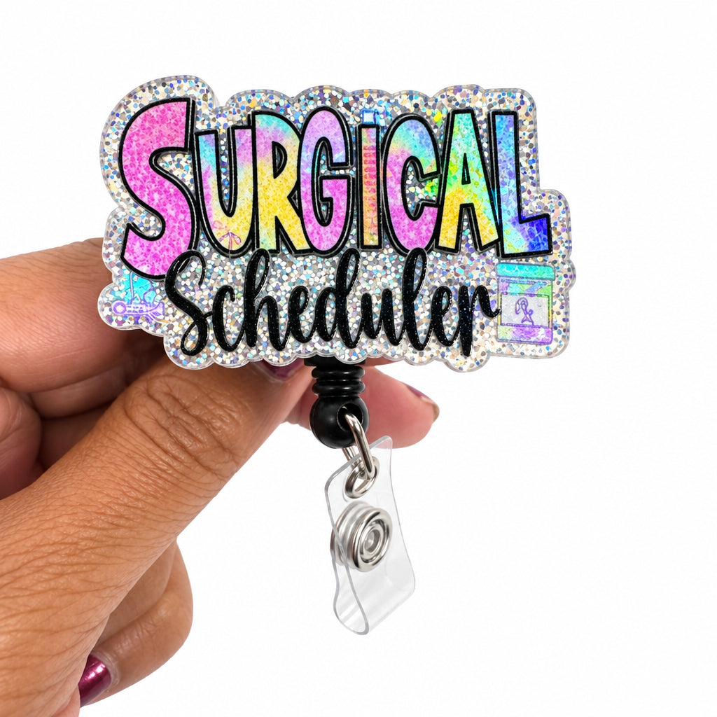 A hand holding a holographic glitter badge reel with the word 'SURGICAL' in colorful bubble letters and 'emergency' in cursive script below it, against a plain white background.