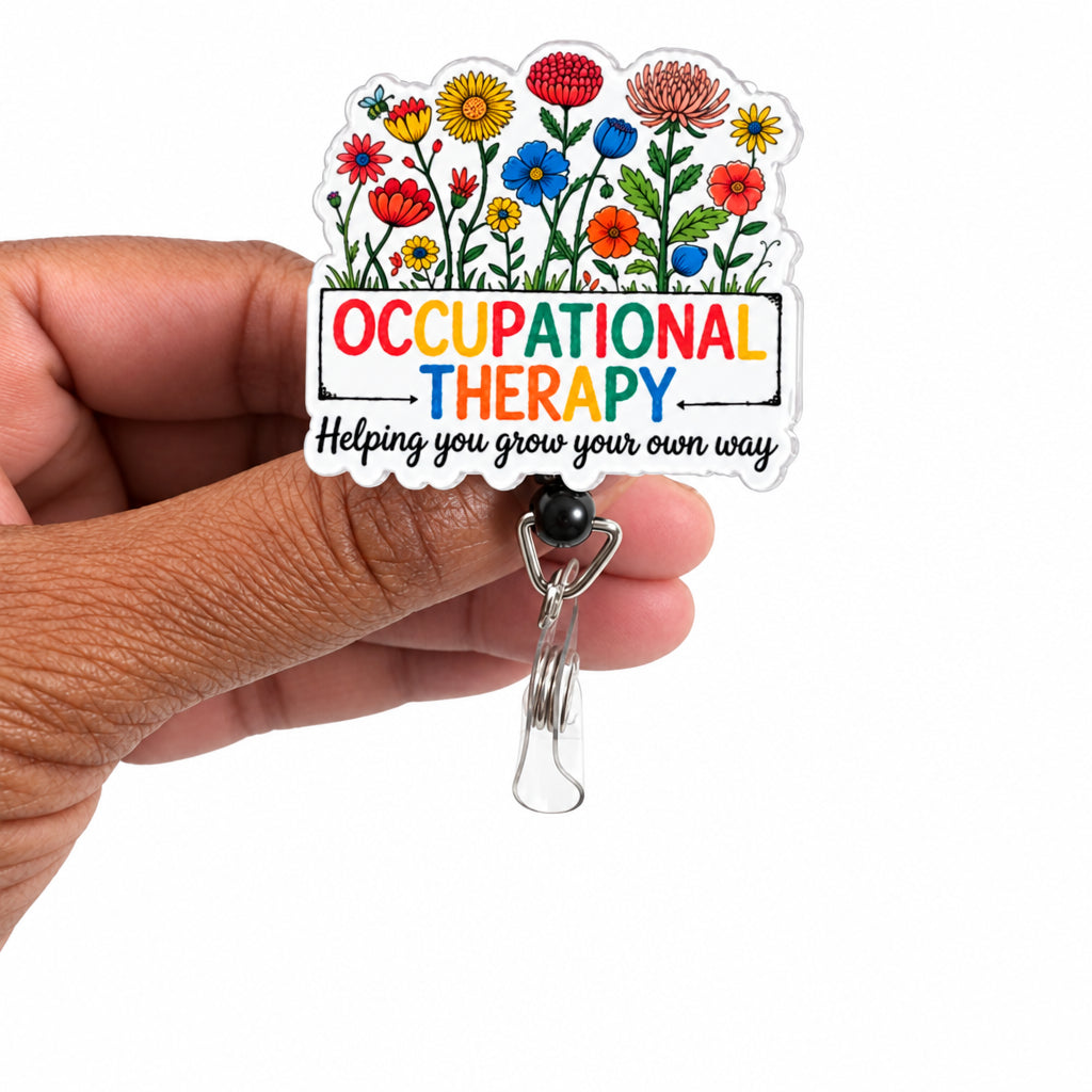 A hand holding a die-cut acrylic badge with colorful flowers and the text 'OCCUPATIONAL THERAPY Helping you grow your own way' attached to a silver metal clip, against a plain white background.