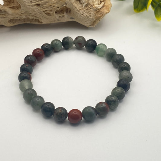 Multicolored beaded bracelet on a white surface with natural wood and green leaves in the background