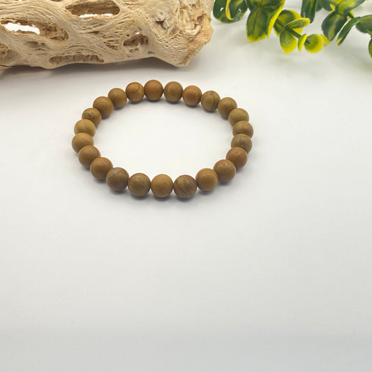Wooden beaded bracelet on a white surface with natural elements in the background