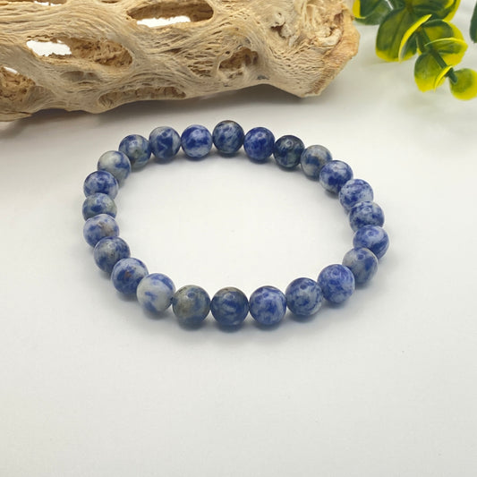 Blue beaded bracelet on a white surface with natural wood and green leaves in the background