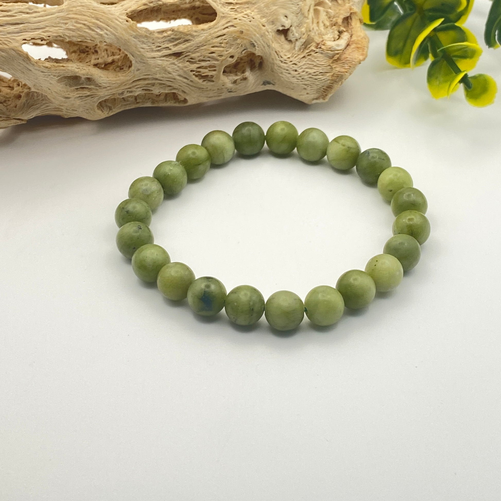 Green beaded bracelet on a white surface with natural wood and green leaves in the background