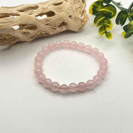 Pink beaded bracelet on a white surface with natural wood and green leaves in the background
