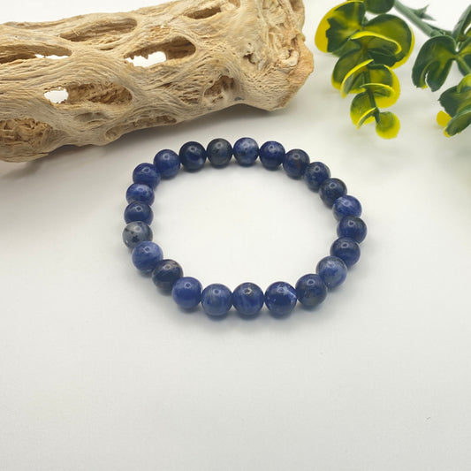 Blue beaded bracelet on a white surface with natural elements in the background