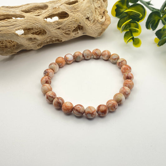 Beaded bracelet on a white surface with natural elements in the background