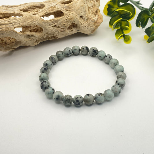 Gray beaded bracelet on a white surface with natural elements in the background