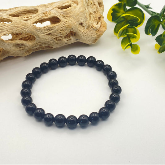 Black beaded bracelet on a white surface with natural elements in the background