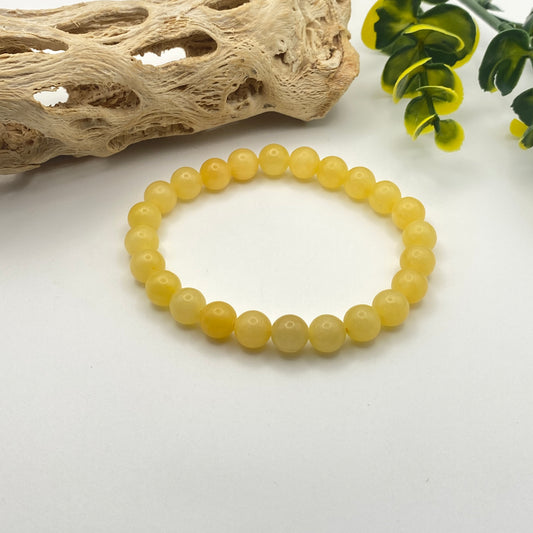 Yellow beaded bracelet on a white surface with natural elements in the background
