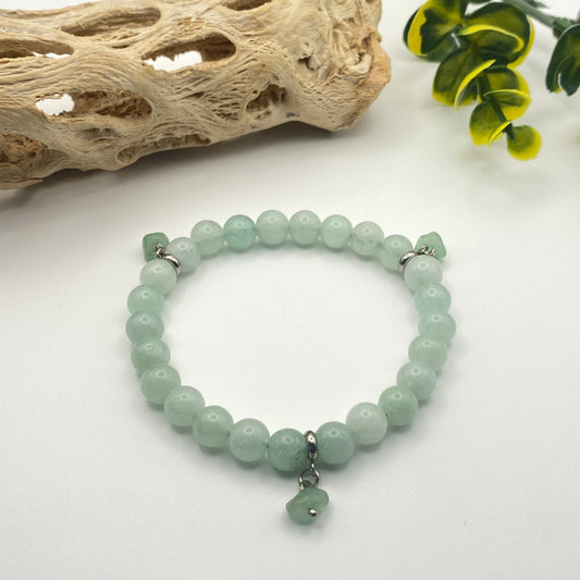 Green beaded bracelet on a white surface with natural elements in the background