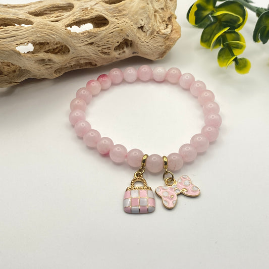 Pink beaded bracelet with charms on a white surface with natural elements.