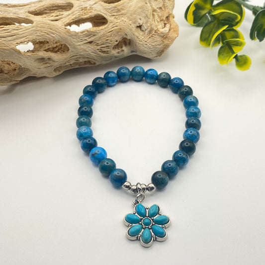 Blue beaded bracelet with a floral charm on a white background