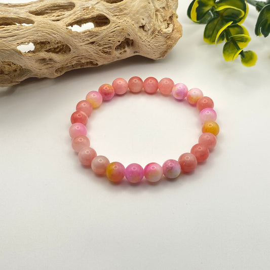 Pink beaded bracelet on a white surface with natural elements