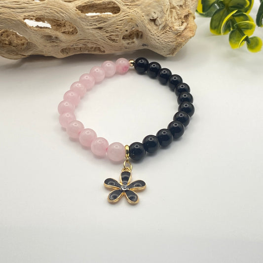 Bracelet with pink and black beads and a flower-shaped charm on a white background