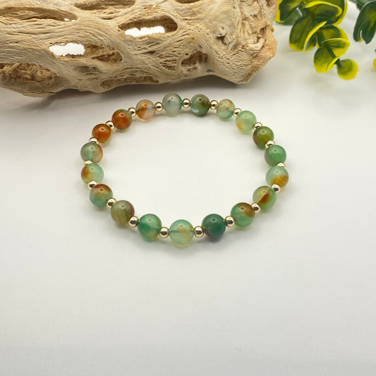 Beaded bracelet with green and gold beads on a white background