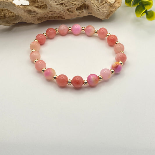 Pink beaded bracelet with gold accents on a light gray background
