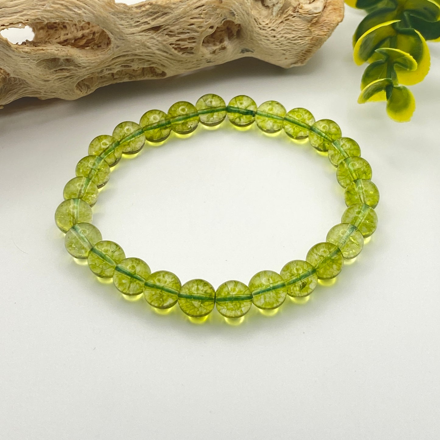 Green beaded bracelet on a white surface with natural elements in the background
