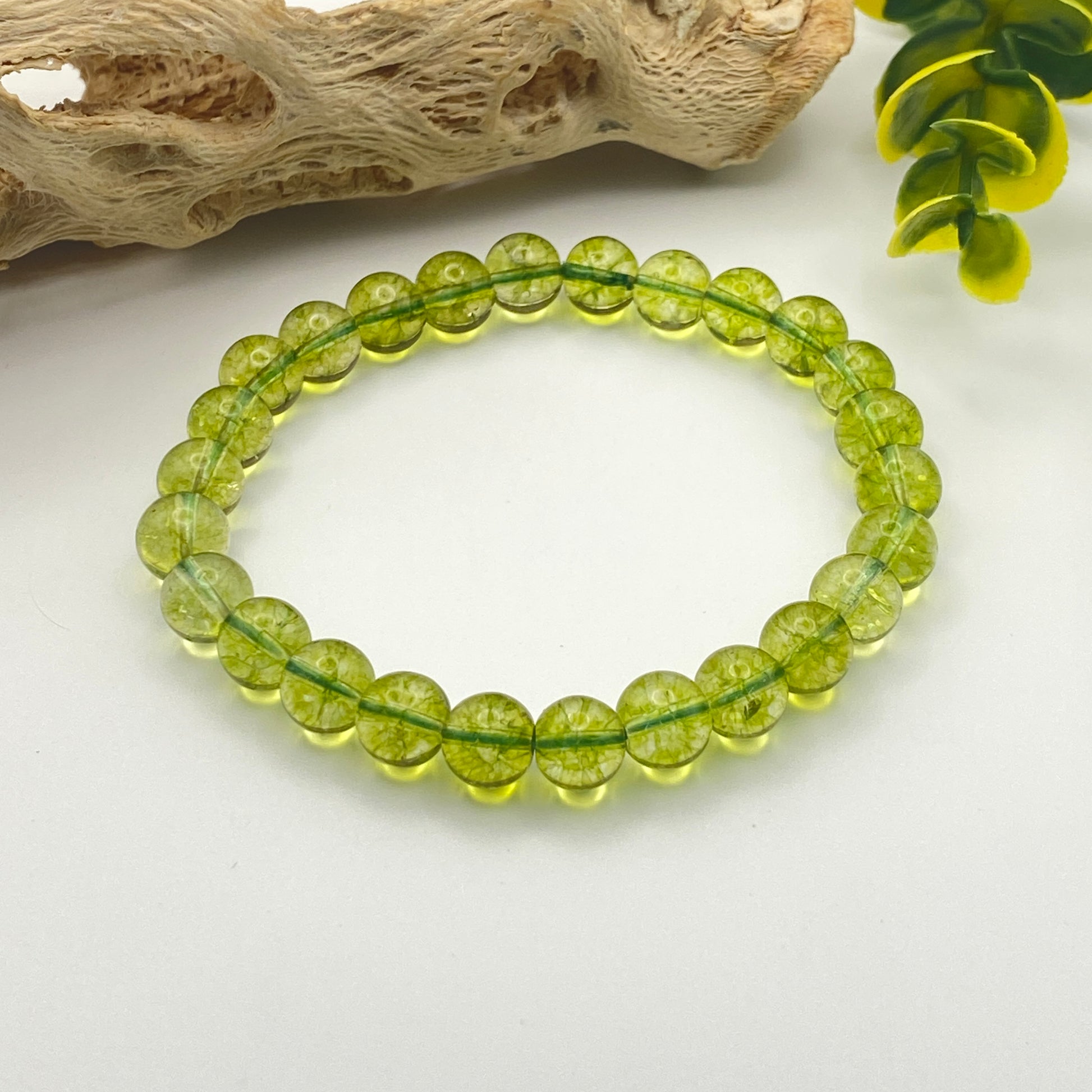 Green beaded bracelet on a white surface with natural elements in the background