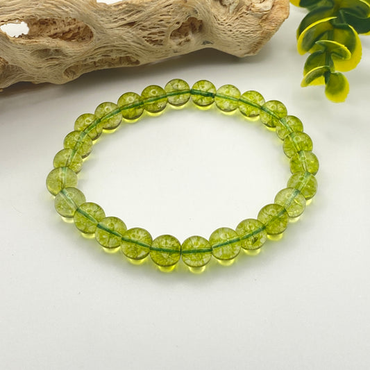 Green beaded bracelet on a white surface with natural elements in the background