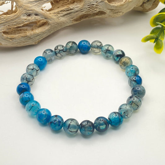 Blue beaded bracelet on a white background with natural elements
