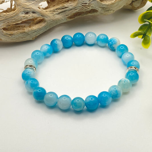 Blue beaded bracelet on a white surface with natural elements in the background