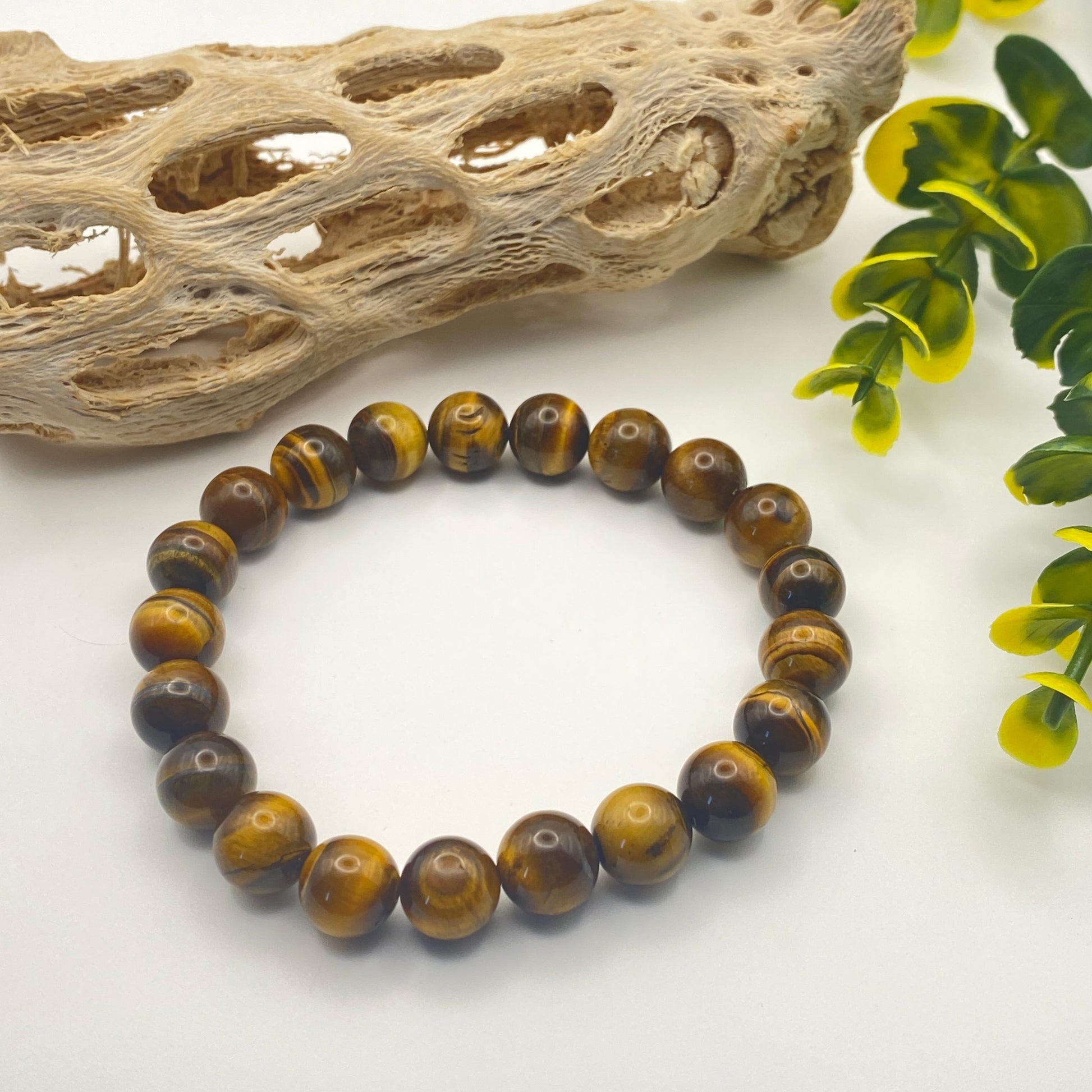 Beaded bracelet with brown and yellow tiger eye stones on a white background with natural elements.