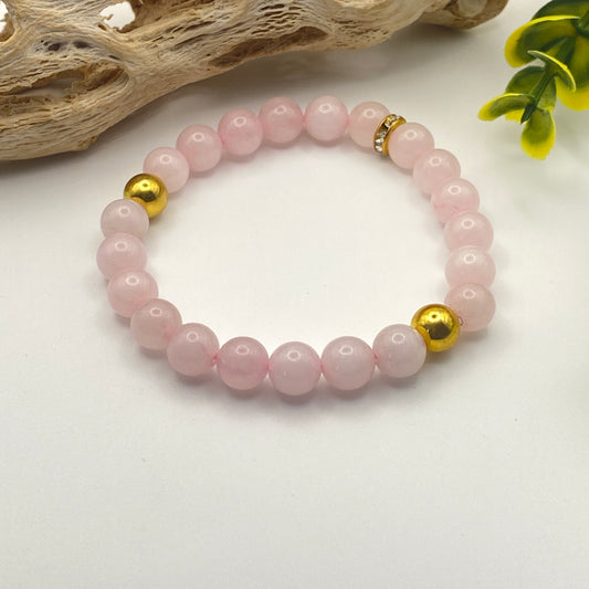 Pink beaded bracelet with gold accents on a white surface with natural elements.