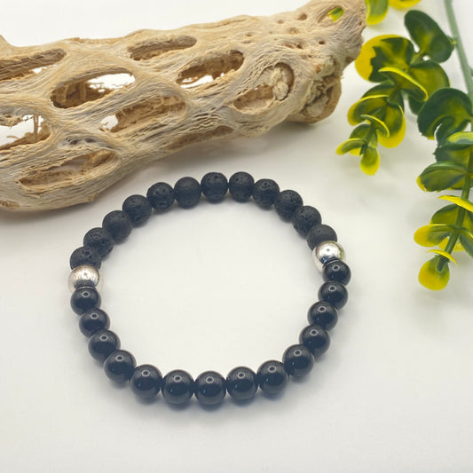 Black beaded bracelet with silver accents on a white background with natural elements.