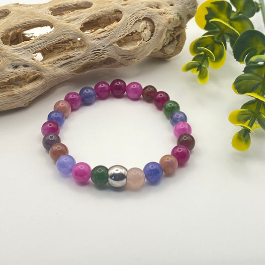 Multicolored beaded bracelet on a white surface with natural elements in the background