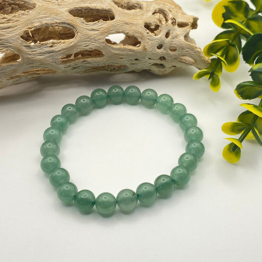 Green beaded bracelet on a white surface with natural elements like driftwood and leaves.