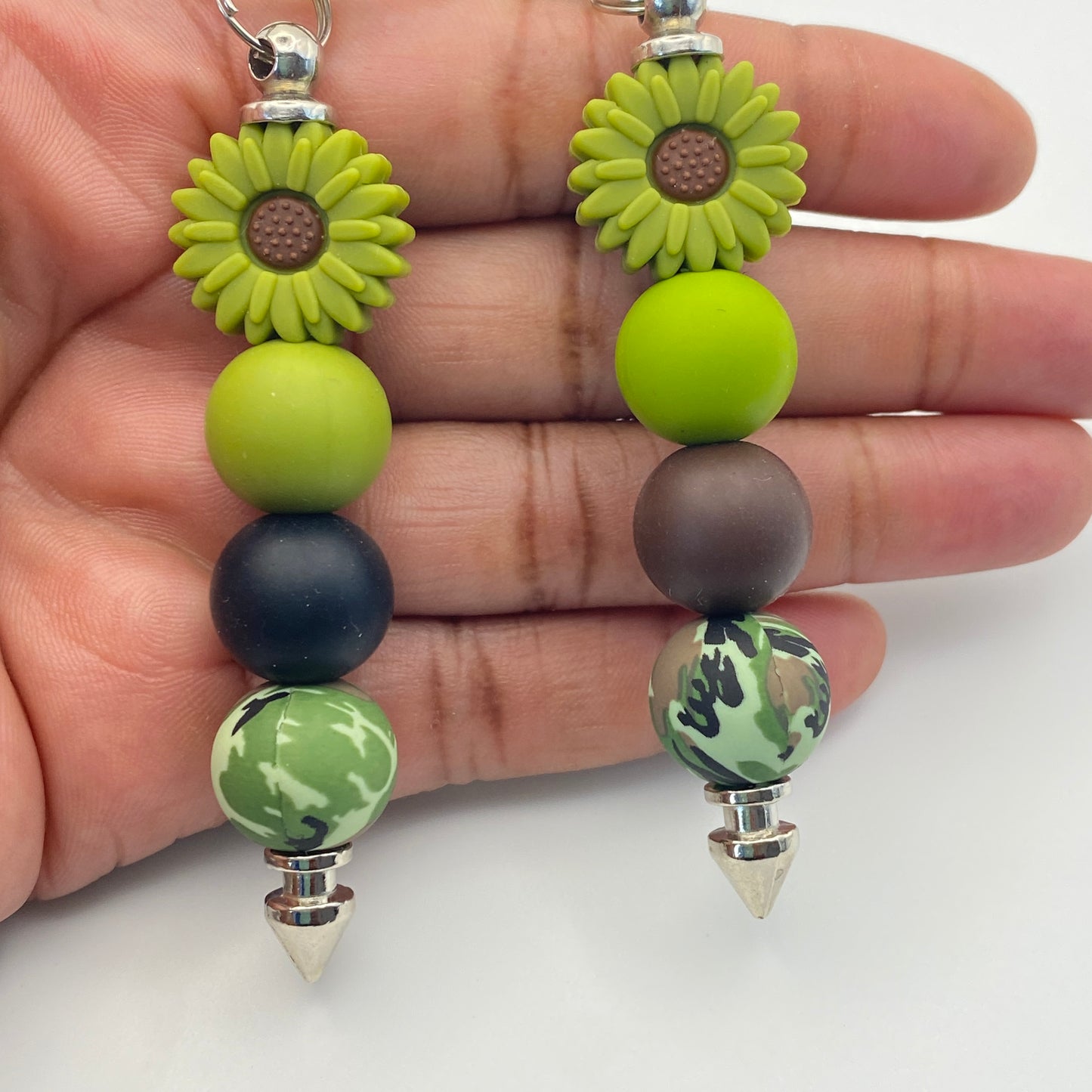 Beaded earrings with green and brown beads held between fingers on a white background