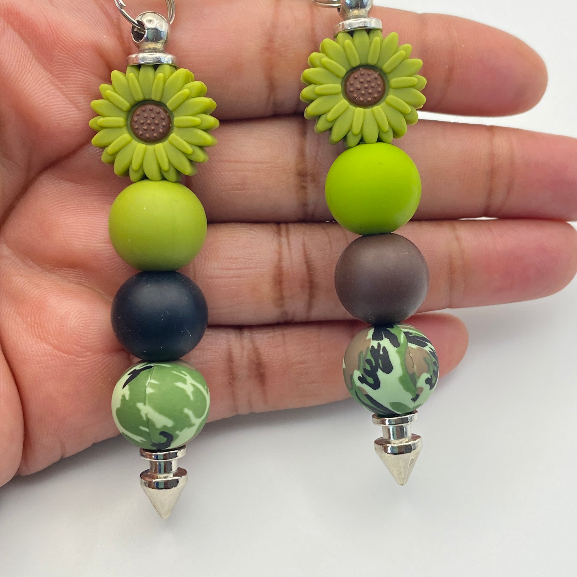 Beaded earrings with green and brown beads held between fingers on a white background