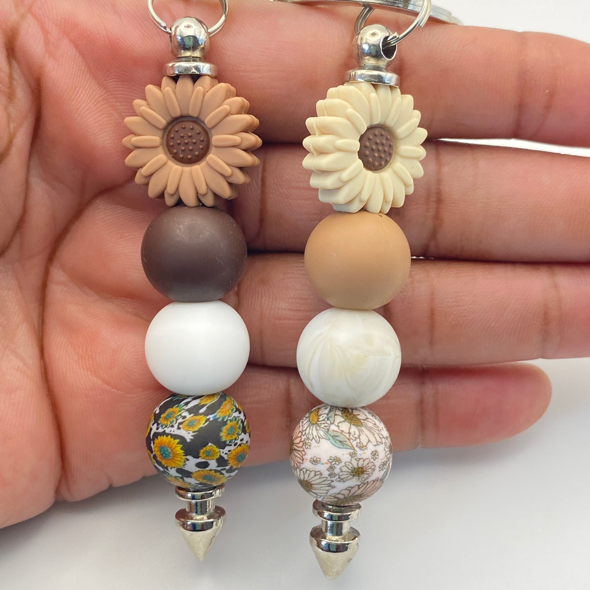 Beaded keychains with floral designs held by a hand on a white background