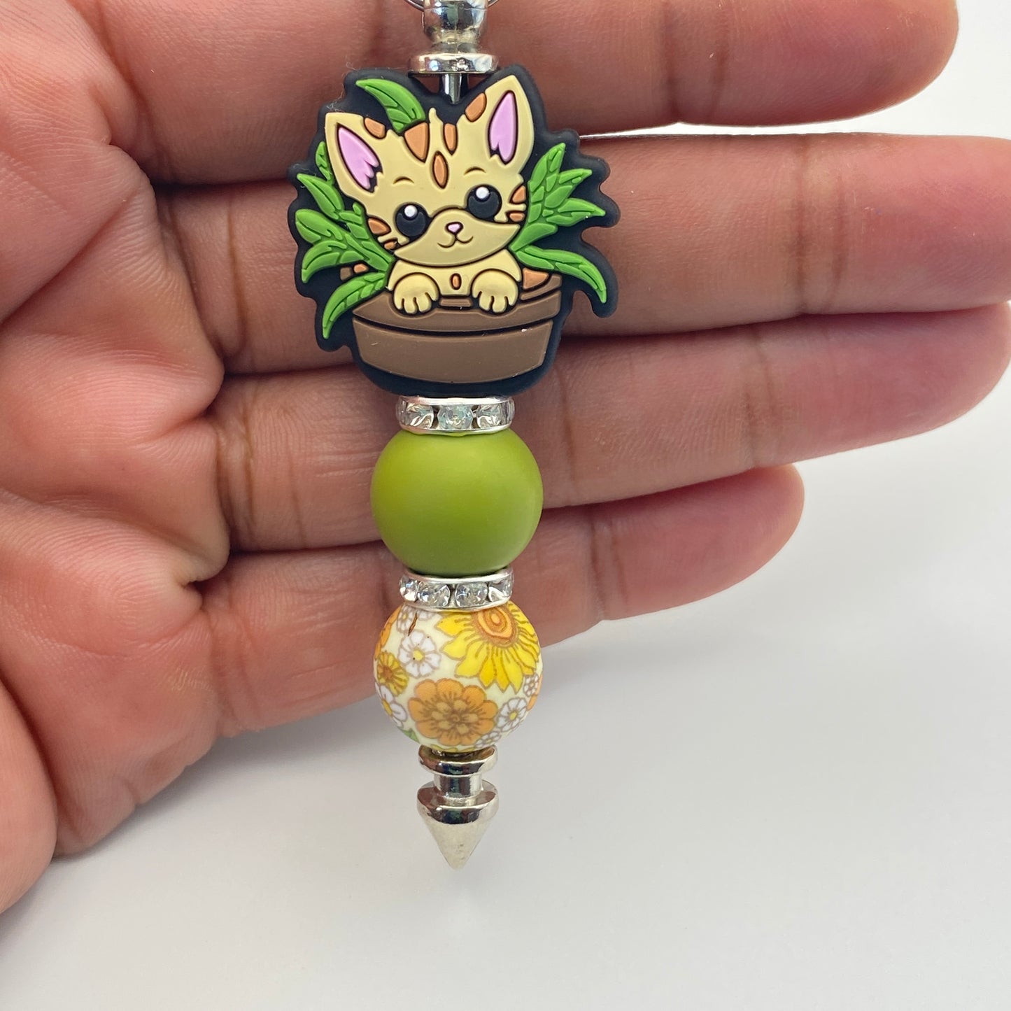 Keychain with a cat design and green bead held in a hand on a white background