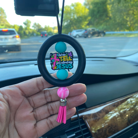 Carabiner with colorful design and tassel held in front of a car's rearview mirror.