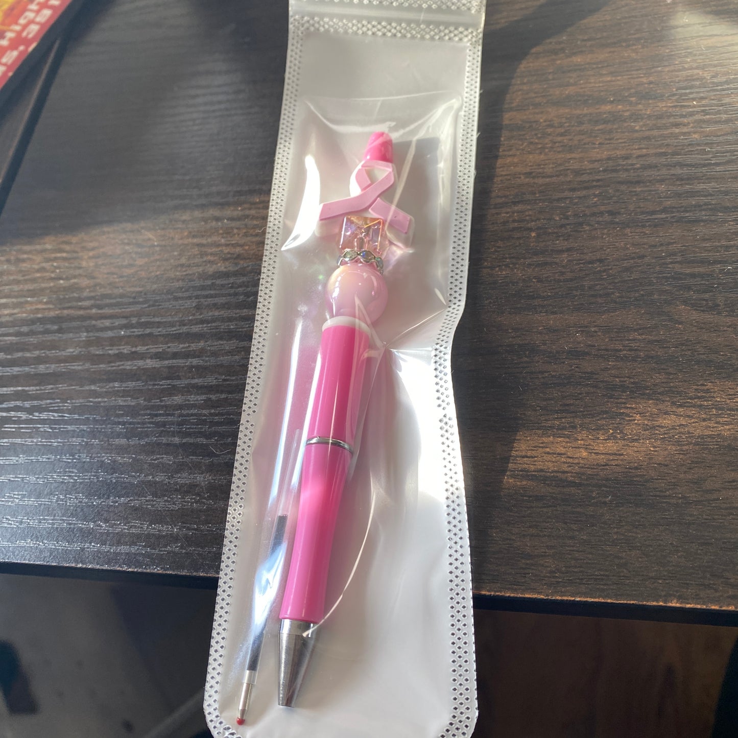Pink pen with a breast cancer awareness ribbon in clear packaging on a wooden surface