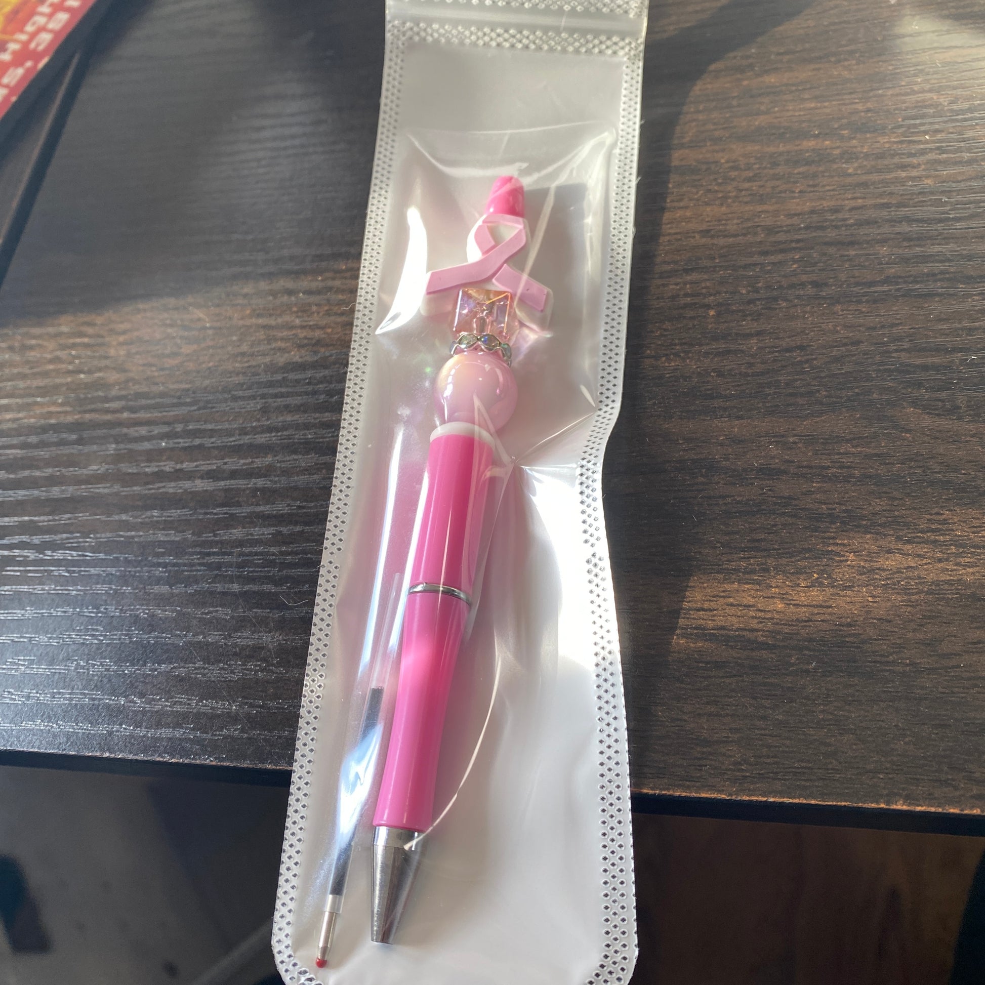 Pink pen with a breast cancer awareness ribbon in clear packaging on a wooden surface