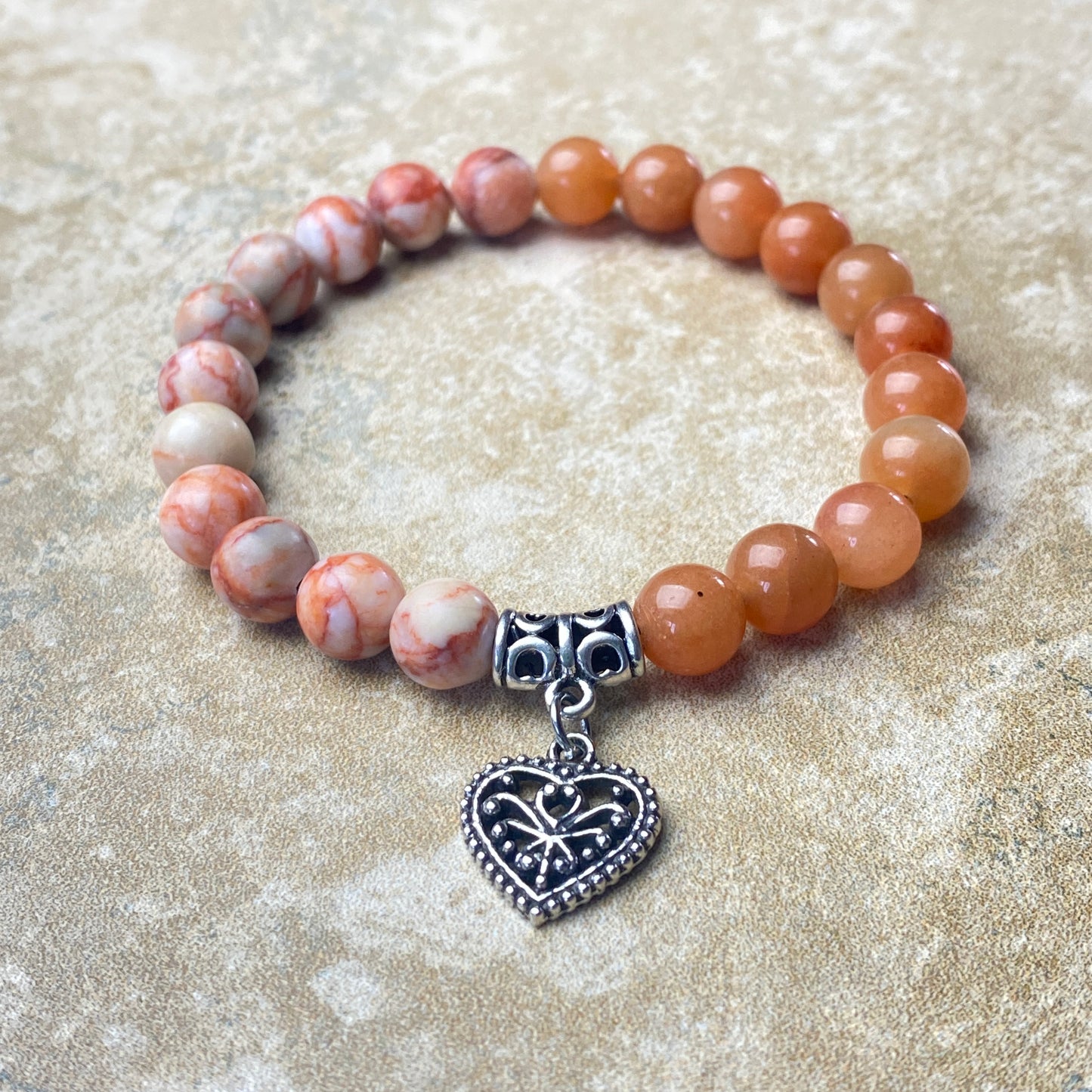 Beaded bracelet with a heart-shaped charm on a sandy background
