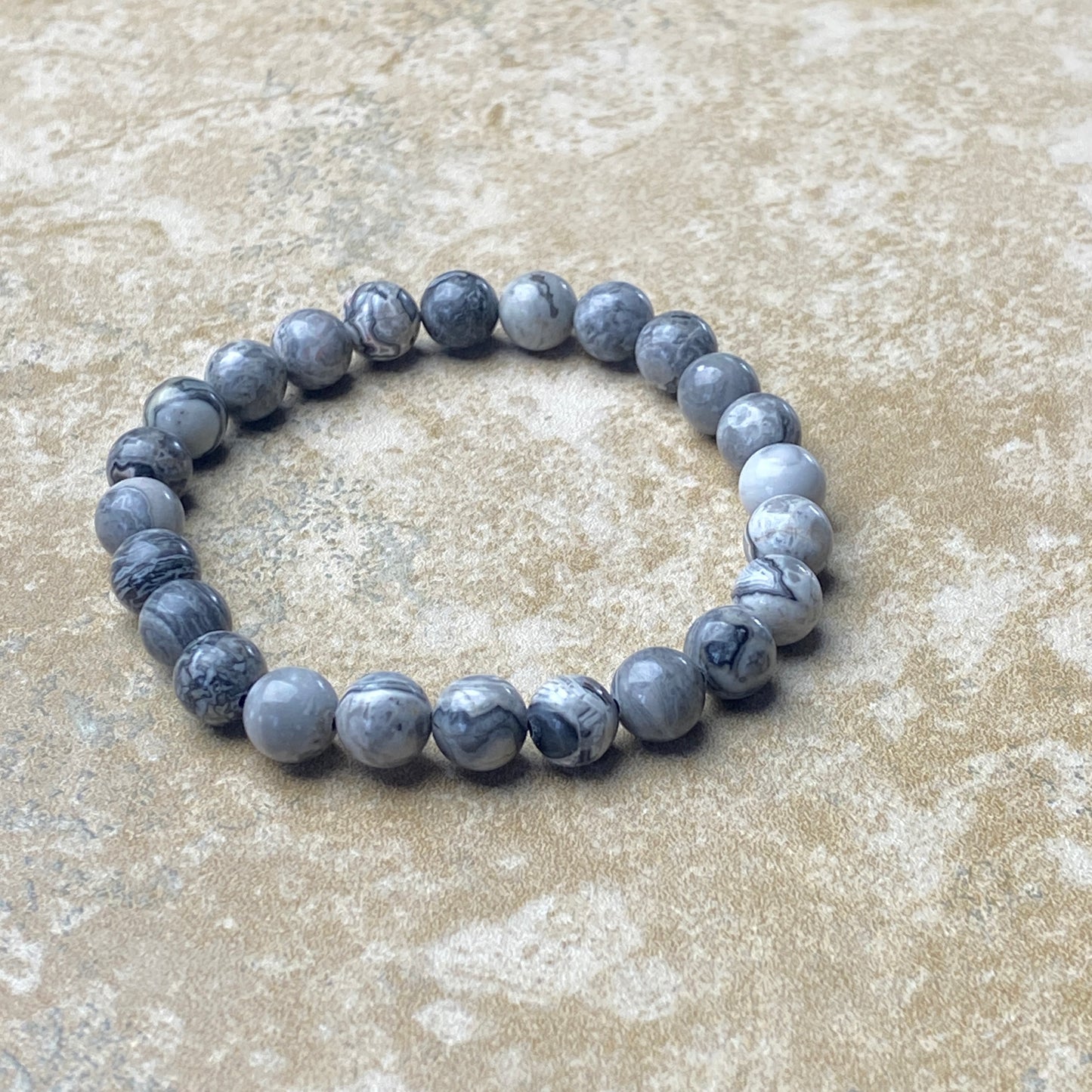 Gray marbled beaded bracelet on a textured beige surface