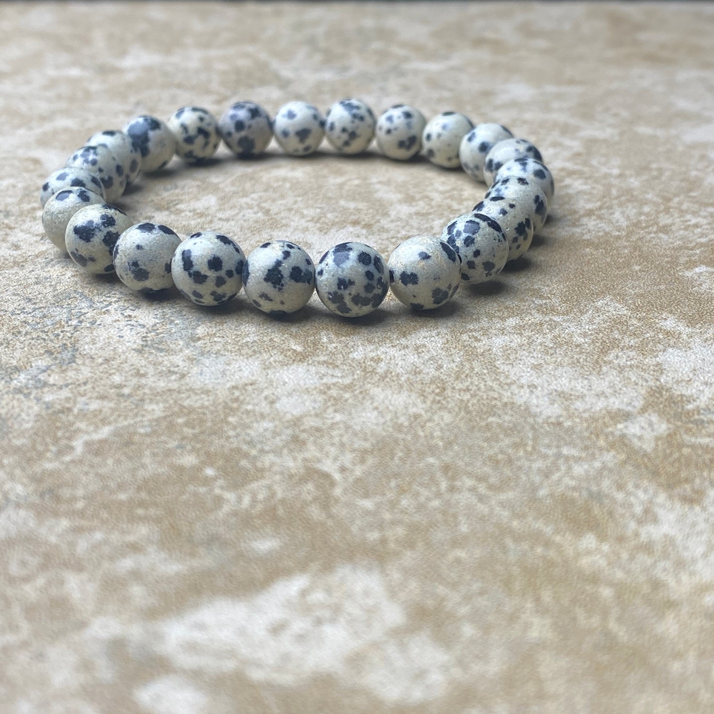 Bracelet with white beads and black spots on a textured beige surface