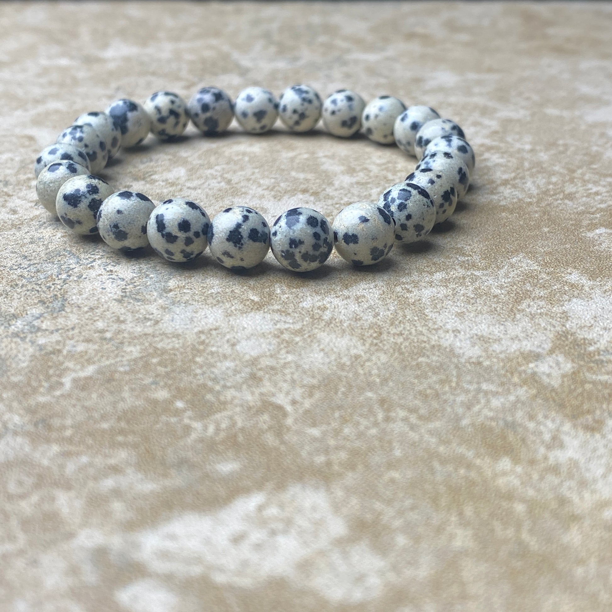 Bracelet with white beads and black spots on a textured beige surface