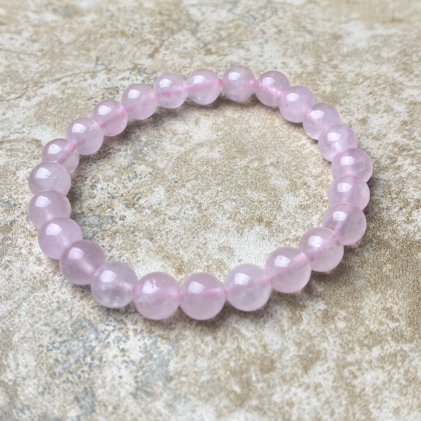 Pink beaded bracelet on a textured beige surface