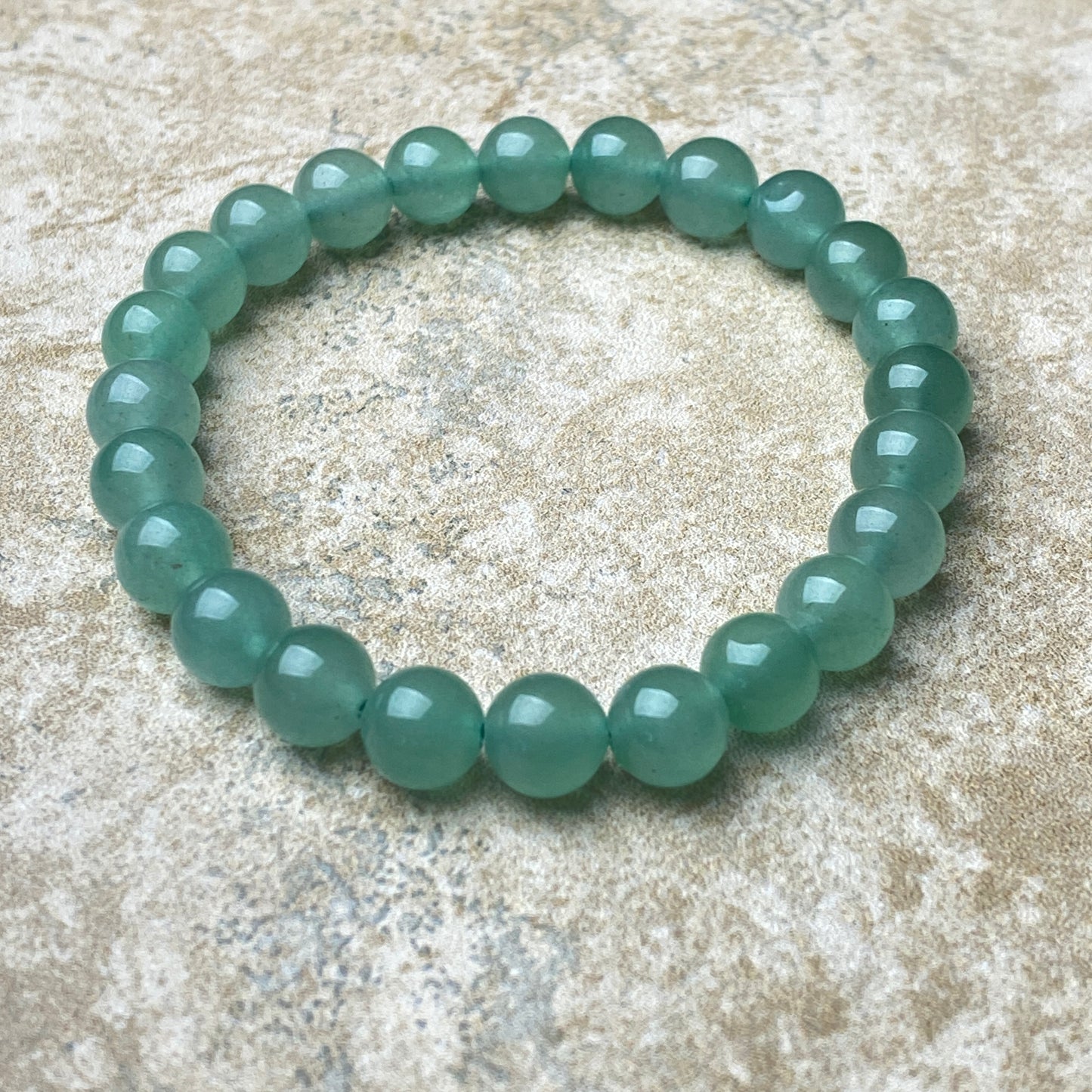 Green beaded bracelet on a textured beige surface