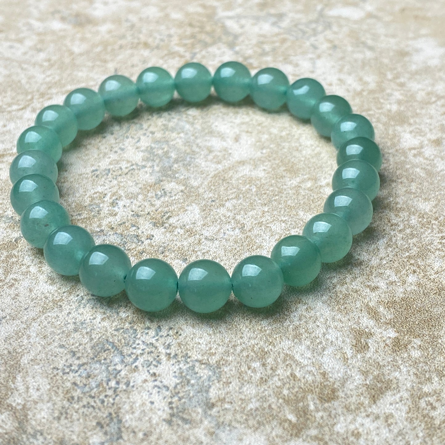 Green beaded bracelet on a textured beige surface